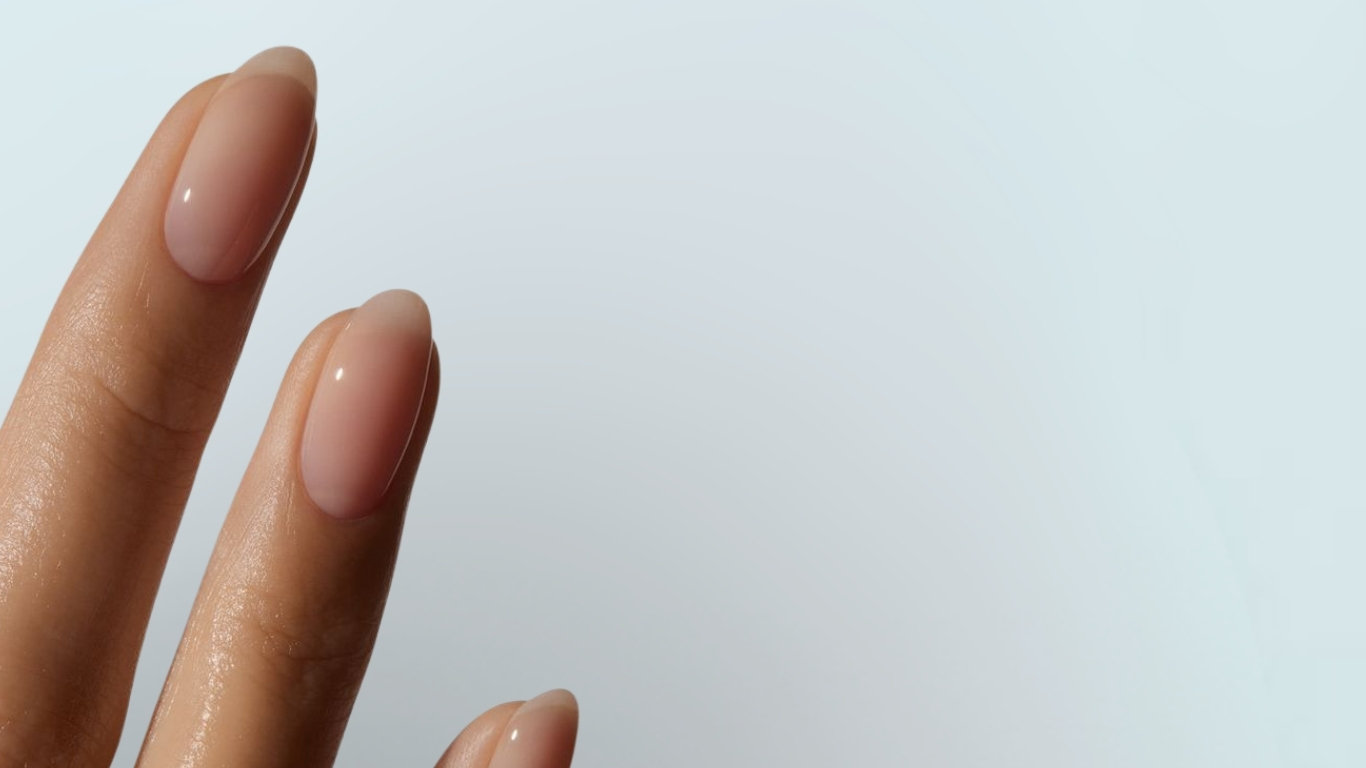 Two fingers with sheer pink nails against neutral background, emphasizing minimal manicure and shine