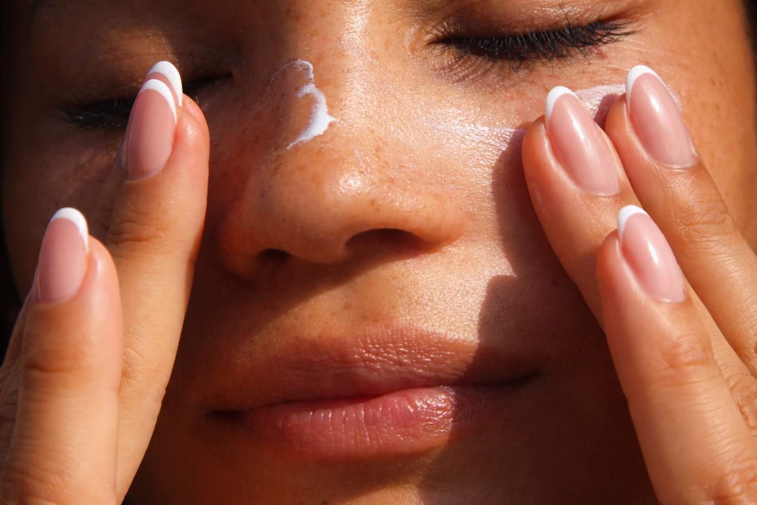 Close-up of freckled skin with closed eyes, showing natural texture and calm skincare moment