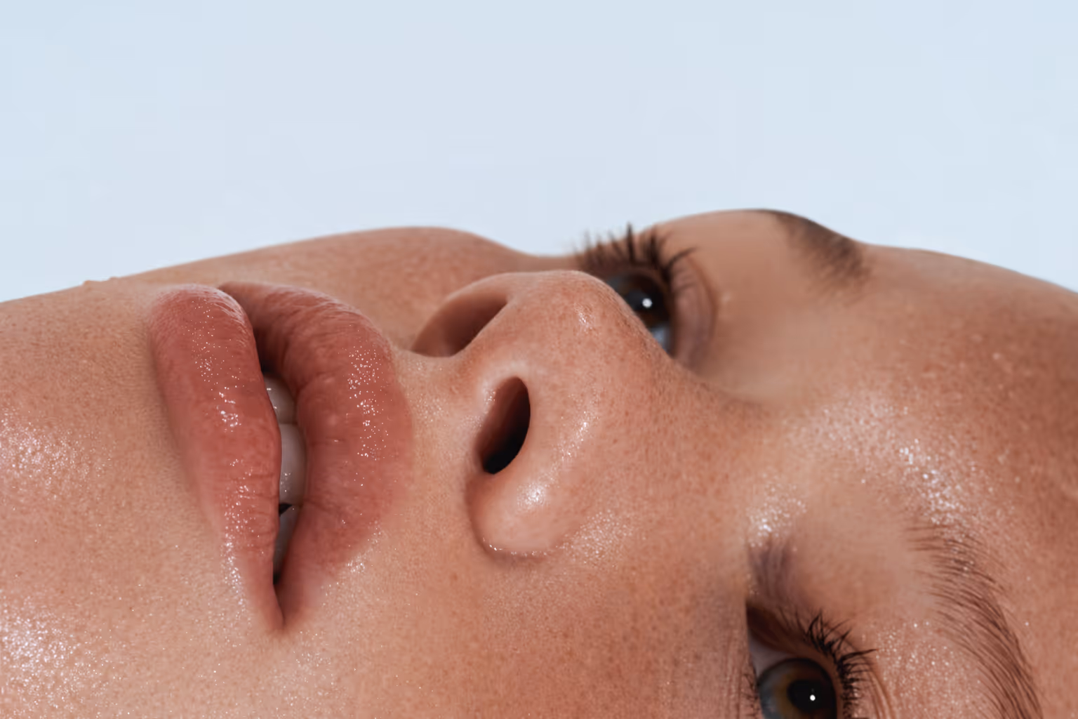 Close-up of dewy skin and natural lips, showing real texture and hydrated glow in soft light