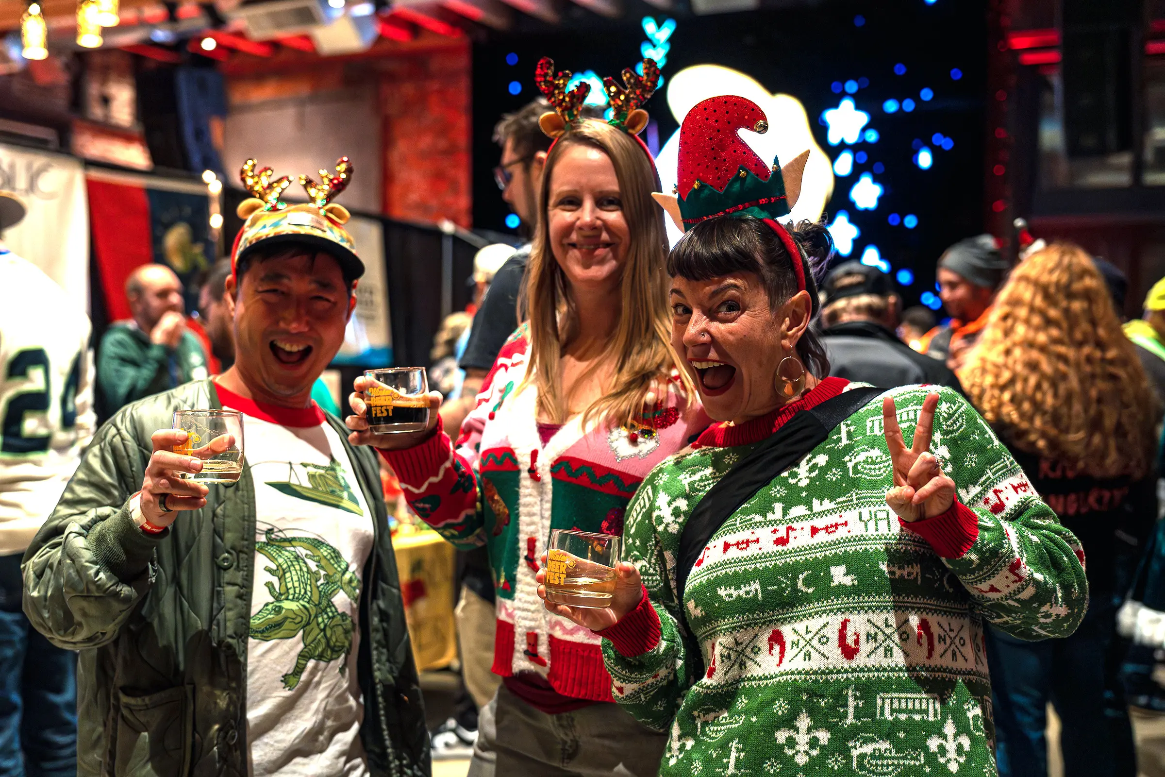 Three attendees in festive holiday sweaters holding beers and smiling at Washington Winter Beer Fest 2025