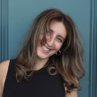 Smiling woman with long wavy hair wearing a sleeveless black top against a teal background.