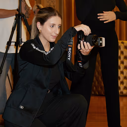 A woman kneeling indoors, holding a Sony camera with a strap, focusing on taking a photo.