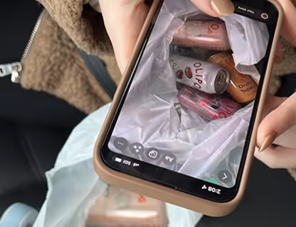 Person holding a phone displaying a photo of a white bag filled with various Olipop soda cans.