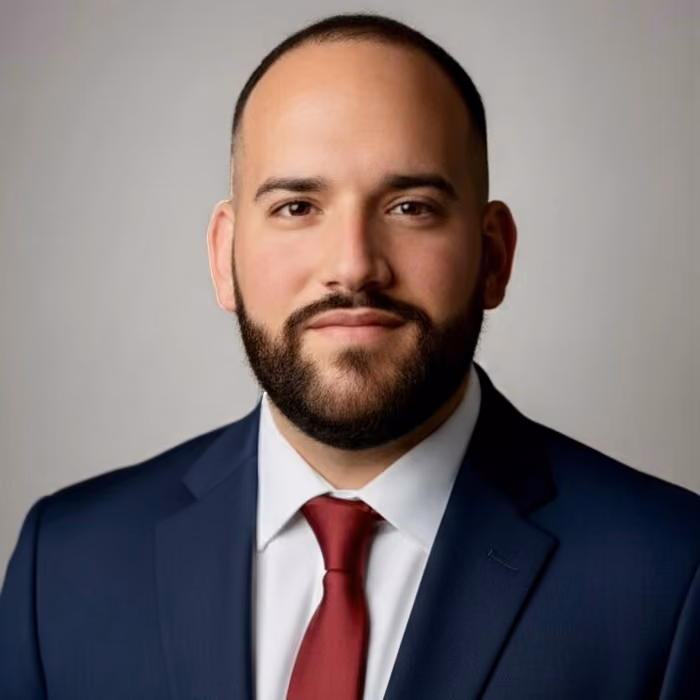 Elder Infante, headshot in a navy suit with a white shirt and red tie.