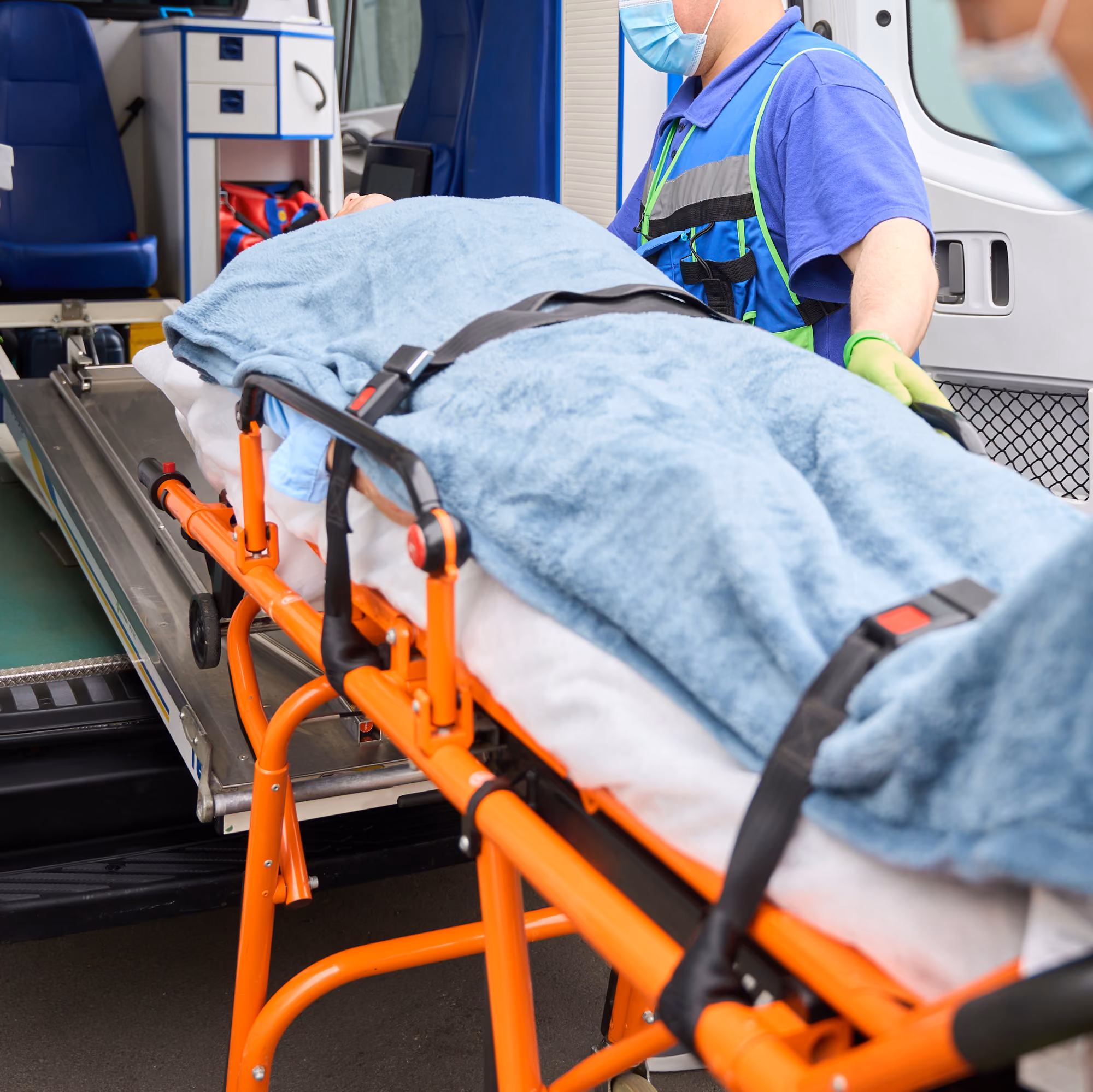 Paramedic loads an empty stretcher with orange frame and blue blanket into the back of an ambulance.