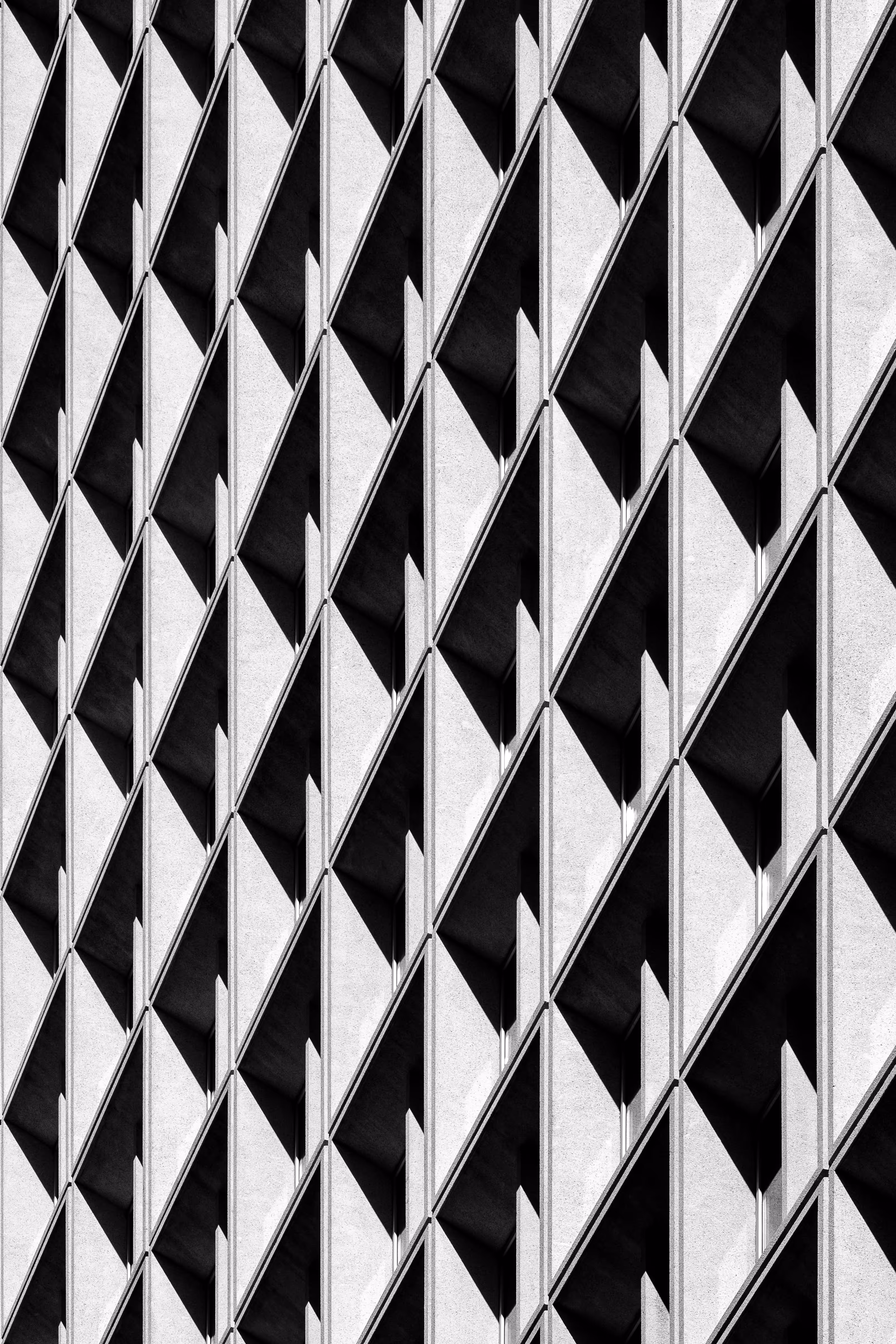 Black and white abstract pattern of a building facade with repetitive angular window shadows.
