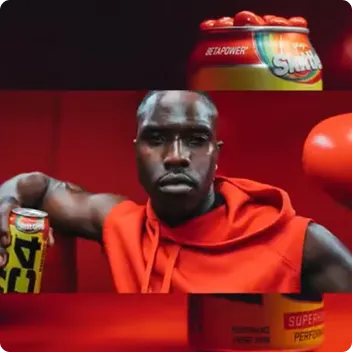 Athletic man wearing a red sleeveless hoodie and boxing glove, holding a yellow energy drink can.