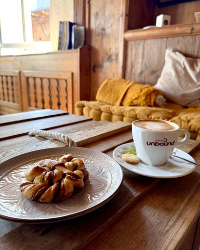 Cup of coffee with latte art and a cookie on a saucer next to a twisted cinnamon pastry on a plate on a wooden table in a cozy cafe.