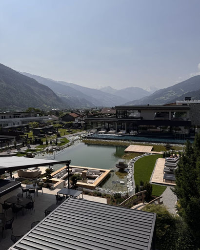 Outdoor view of a modern resort with a pond, seating areas, and mountains in the background under a clear sky.