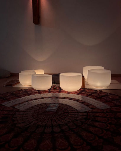 Seven illuminated frosted glass singing bowls arranged on a mat with tarot cards spread out on a patterned rug in a dimly lit room.