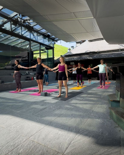 Group of people standing on yoga mats outdoors holding hands and practicing yoga.