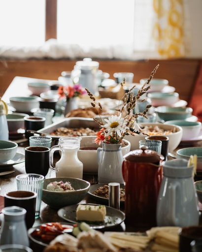 Table set with various bowls, mugs, pitchers, and a central vase with wildflowers in a cozy dining room.