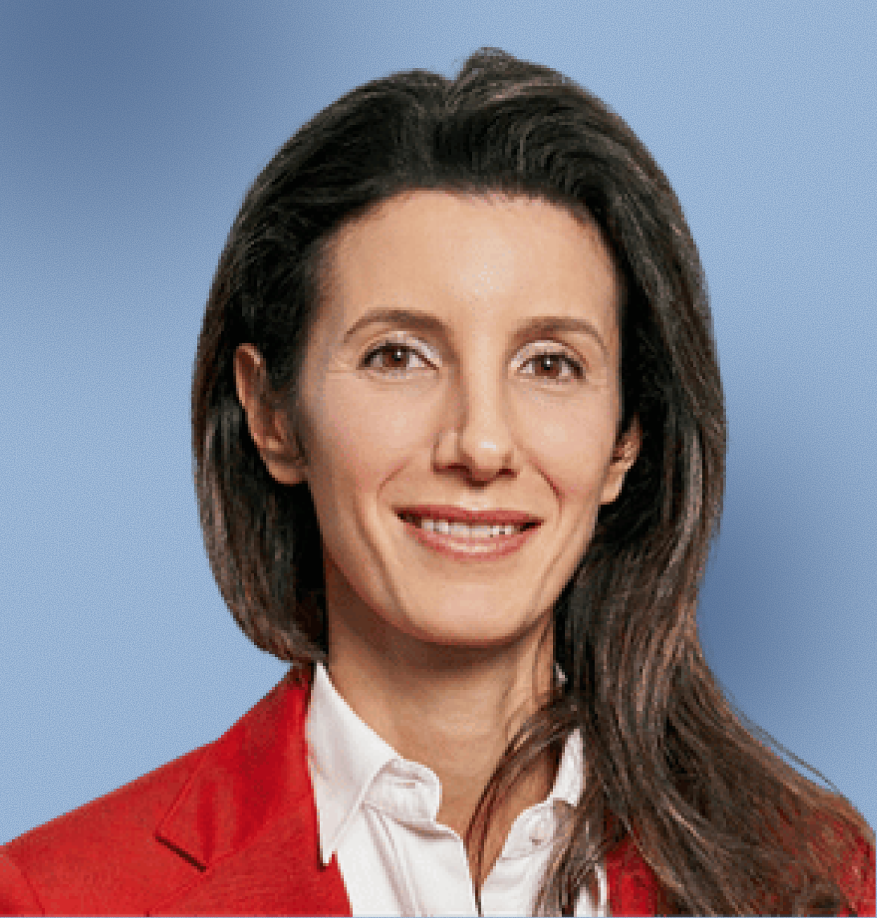 Smiling woman with long brown hair wearing a red blazer and white shirt against a blue background.