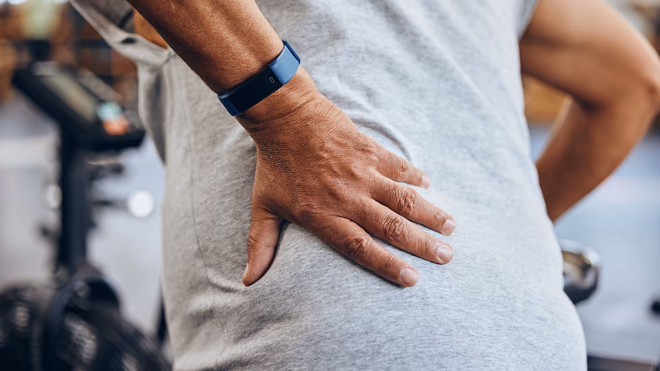 Close-up of a person holding their lower back, wearing a fitness tracker on their wrist.