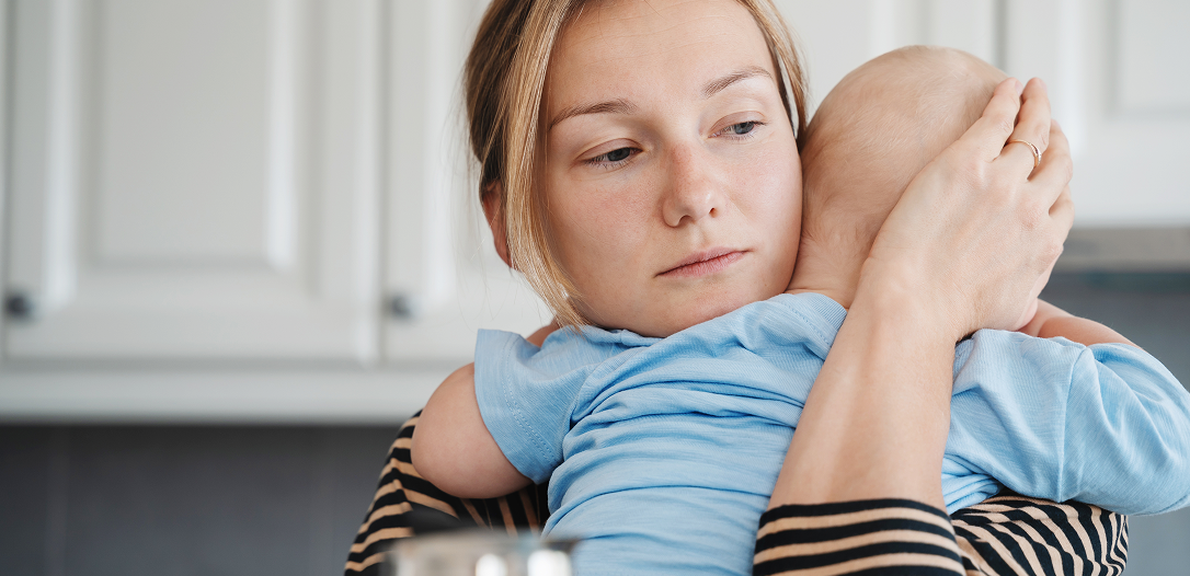 A woman holding and comforting a baby dressed in a blue shirt in a kitchen setting.
