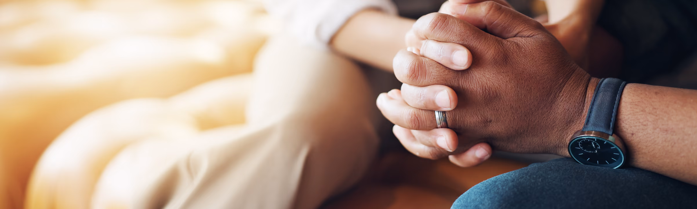 Two people holding hands, one wearing a wedding ring and a black watch, sitting closely.