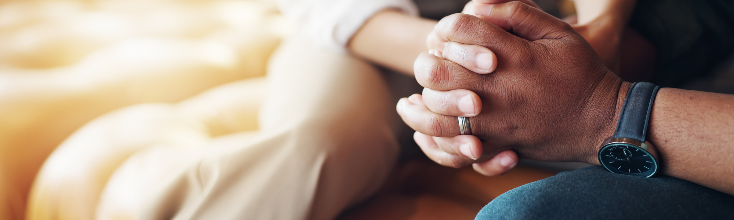 Two people holding hands, one wearing a wedding ring and a black watch, sitting closely.
