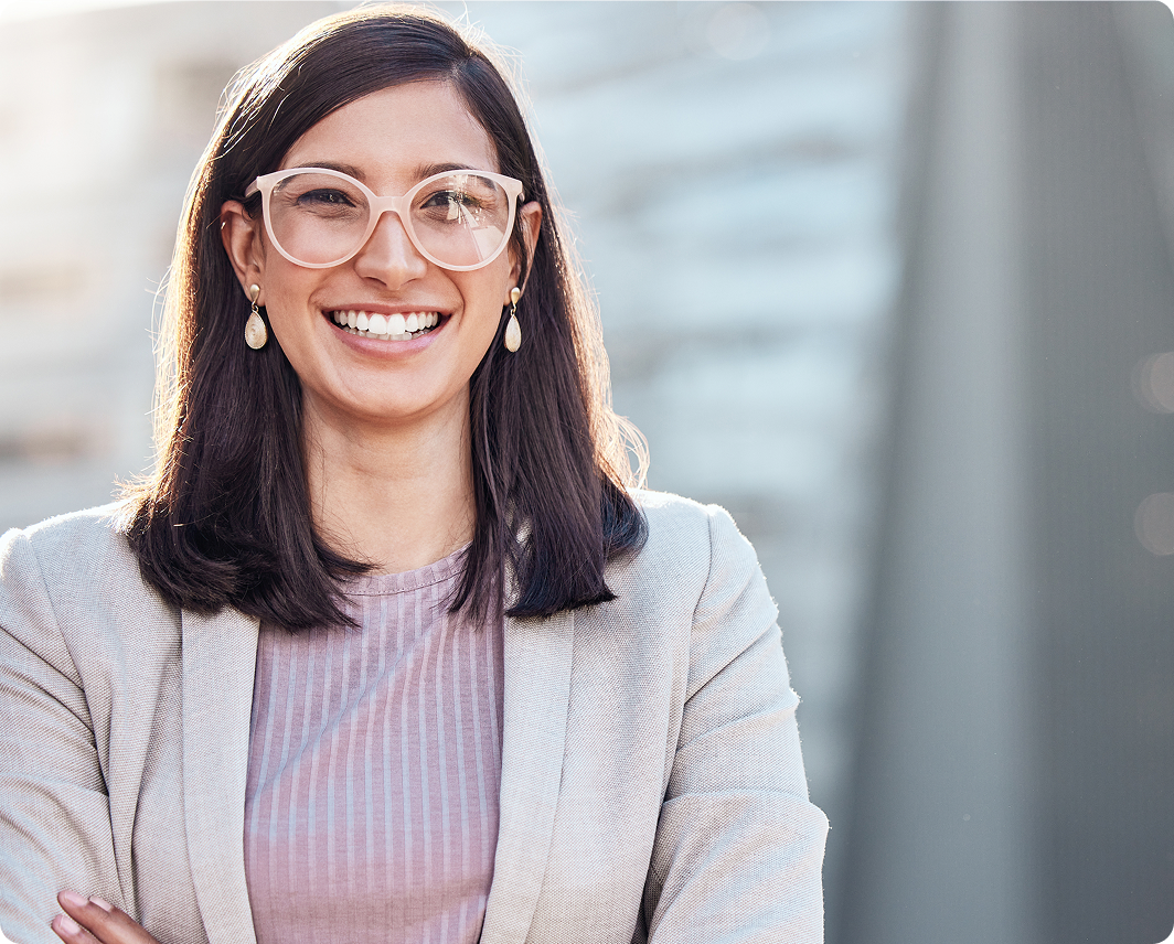 Smiling woman with shoulder-length dark hair wearing glasses, earrings, a light blazer, and a pink striped top.