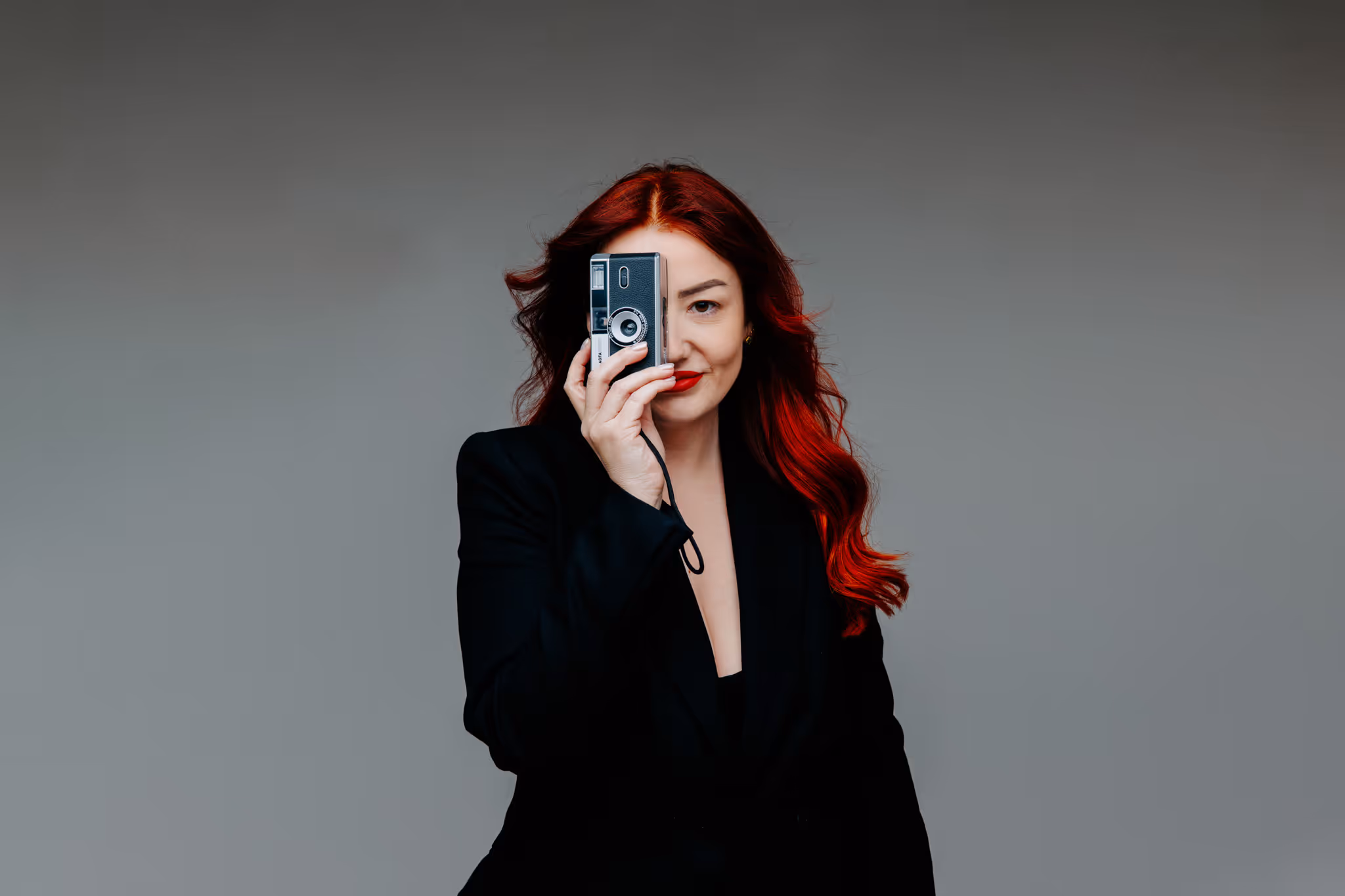 Portret Marine Buhin koja drži mali retro fotoaparat ispred desnog oka, upečatljiva studijska fotografija, landscape format.