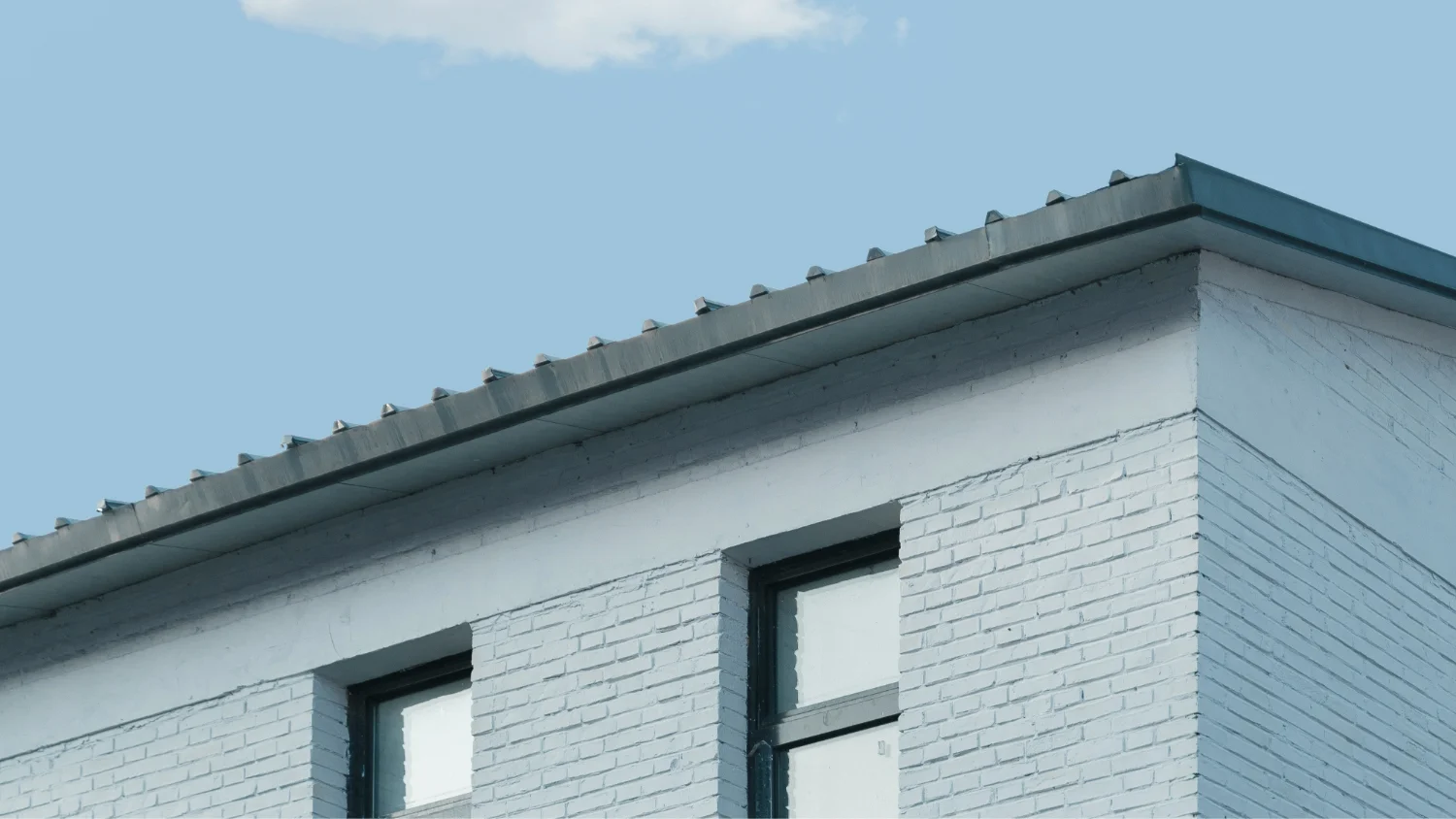 Corner of a white brick building with two windows under a clear blue sky.
