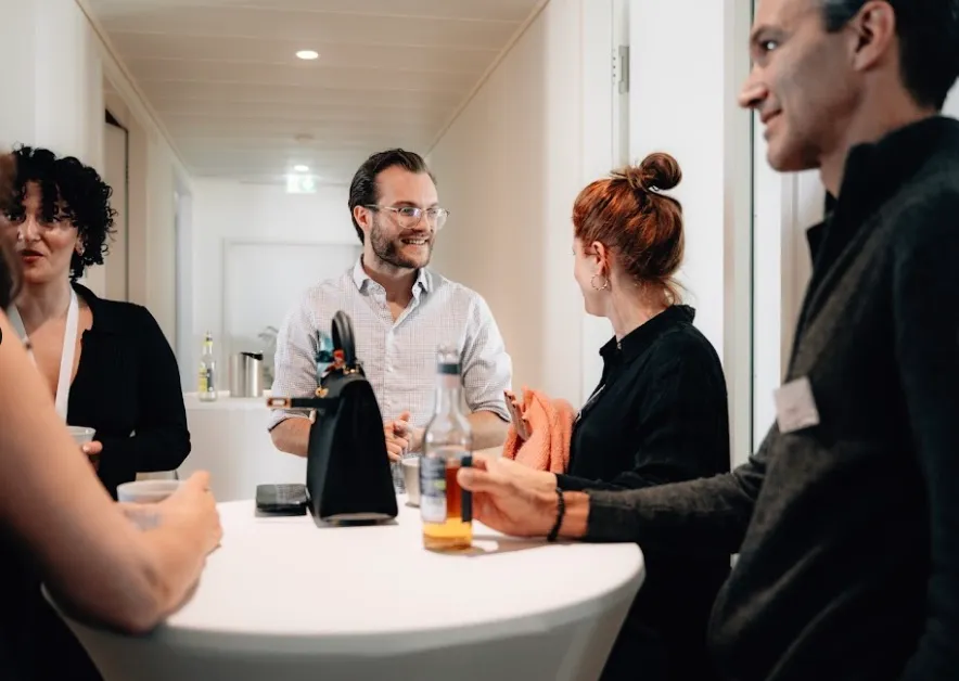 Small group of people casually networking around a high table with drinks, highlighting the supportive and community-focused environment of IT and AI (KI) training for digital commerce