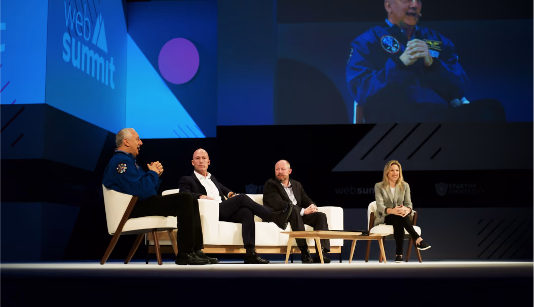 Four people seated on stage during a Web Summit panel discussion with a large screen behind them.