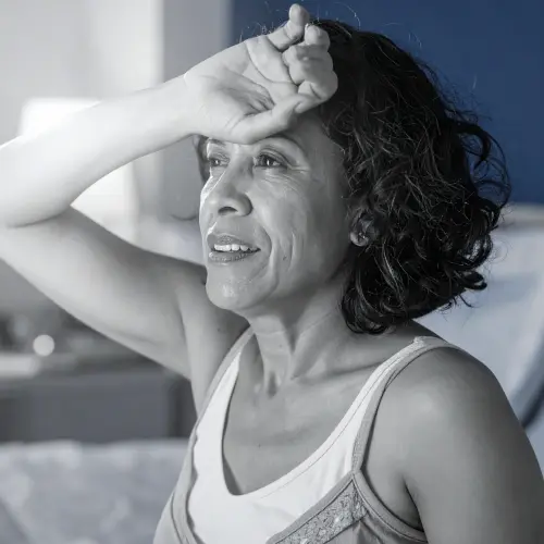 Black and white photo of a woman wiping her forehead, related to menopause night sweats