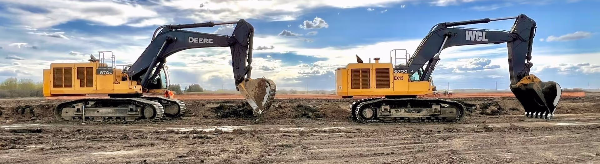 Two large yellow and black excavators on a construction site with a partly cloudy sky.