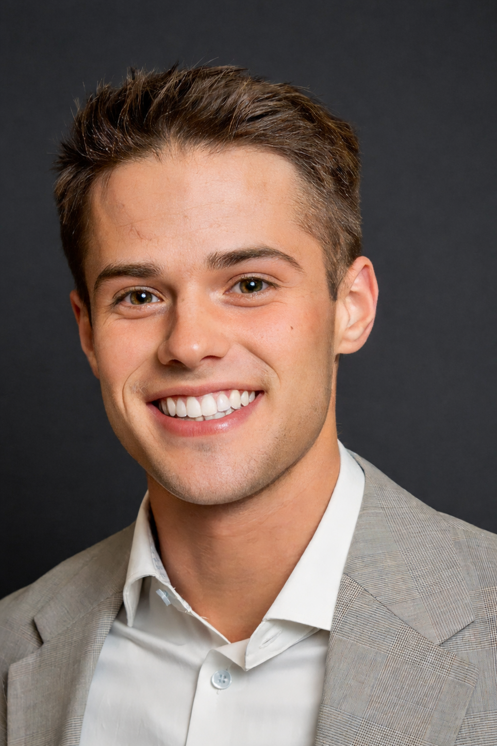 Smiling bald man with light beard and glasses wearing a gray knit sweater against a light gray background.