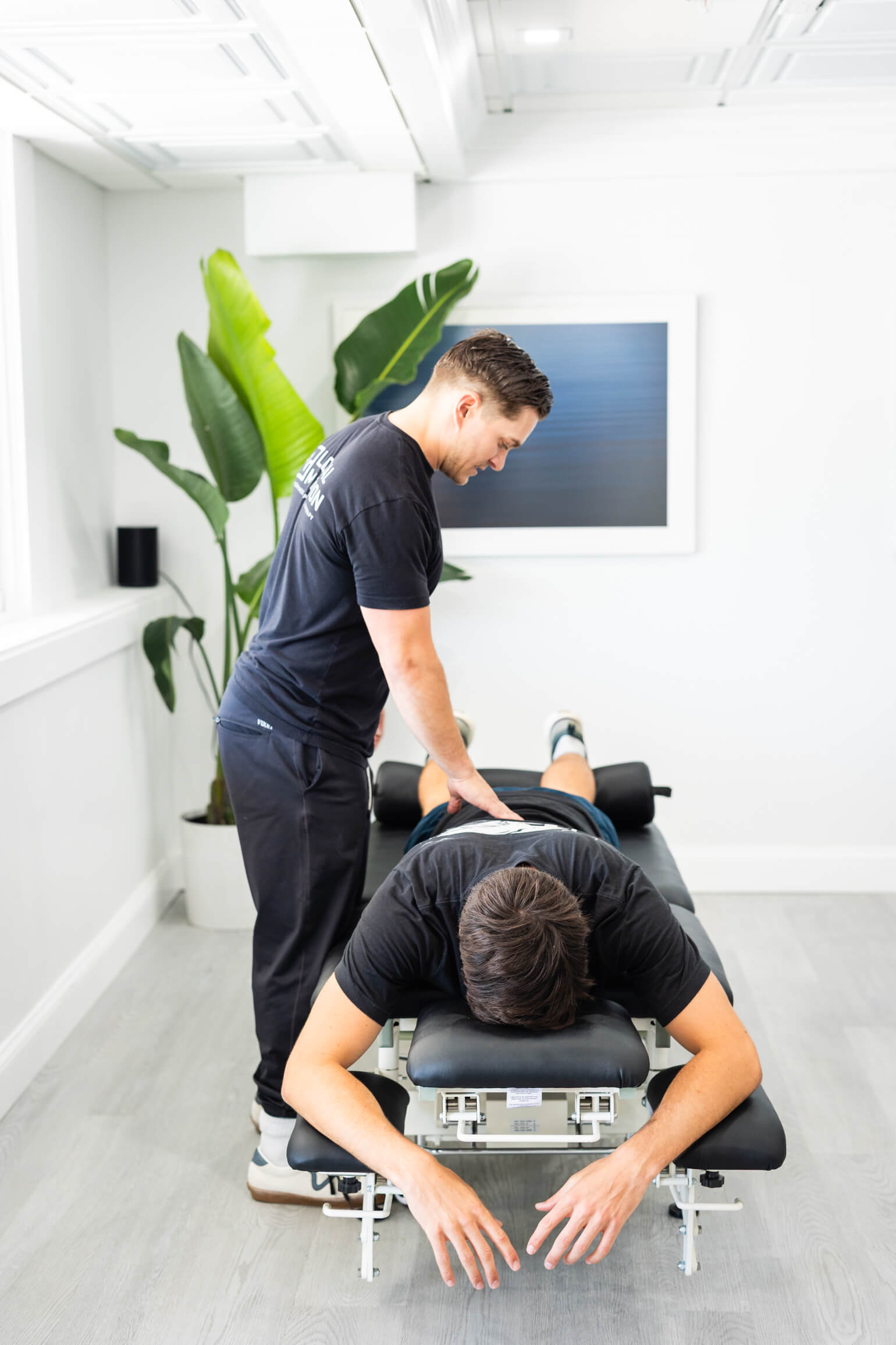 Therapist providing a back massage to a person lying face down on a treatment table in a bright room.