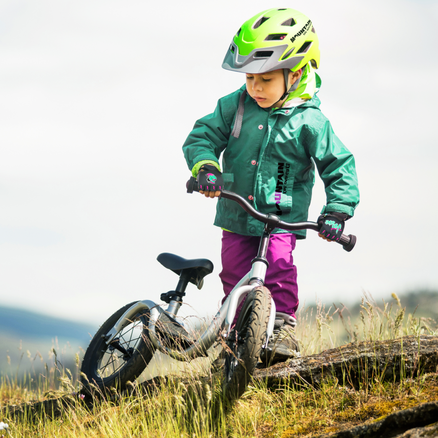 A child wearing a green Mountain Kids Outfitters jacket is getting ready to ride her bike.