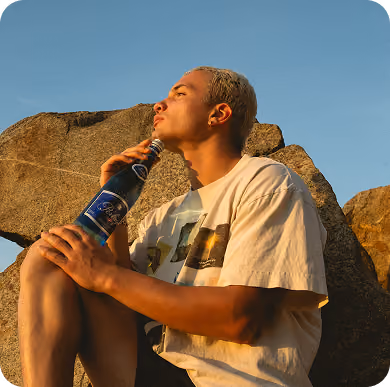 Hombre bebiendo de una botella sobre las rocas
