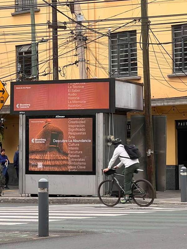 Bloomberg Connects poster at a street kiosk with a cyclist passing