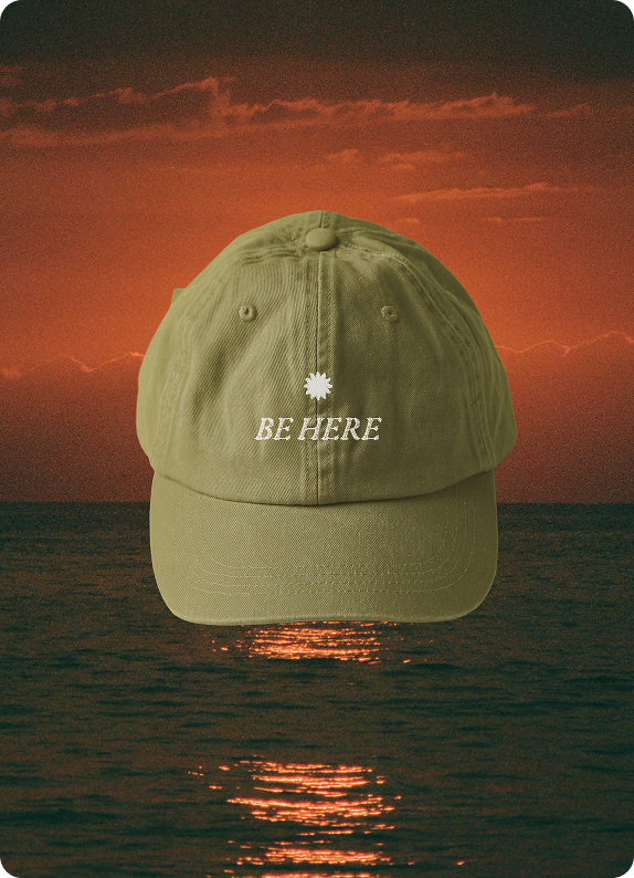 La Joya 'Be Here' cap in olive over a sunset seascape