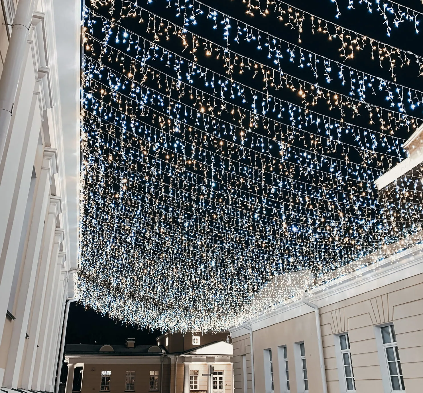 Outdoor courtyard at night with strings of warm white and cool white fairy lights hanging overhead between buildings.