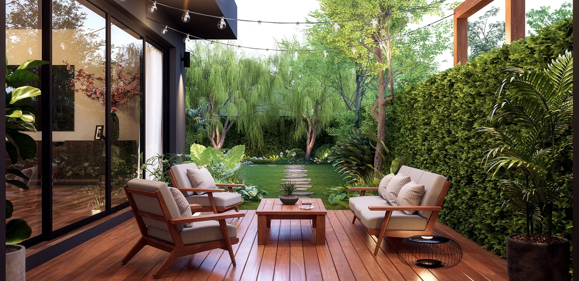 Outdoor patio with wooden deck, cushioned chairs, a coffee table, string lights, and greenery surrounding a walkway to a garden.