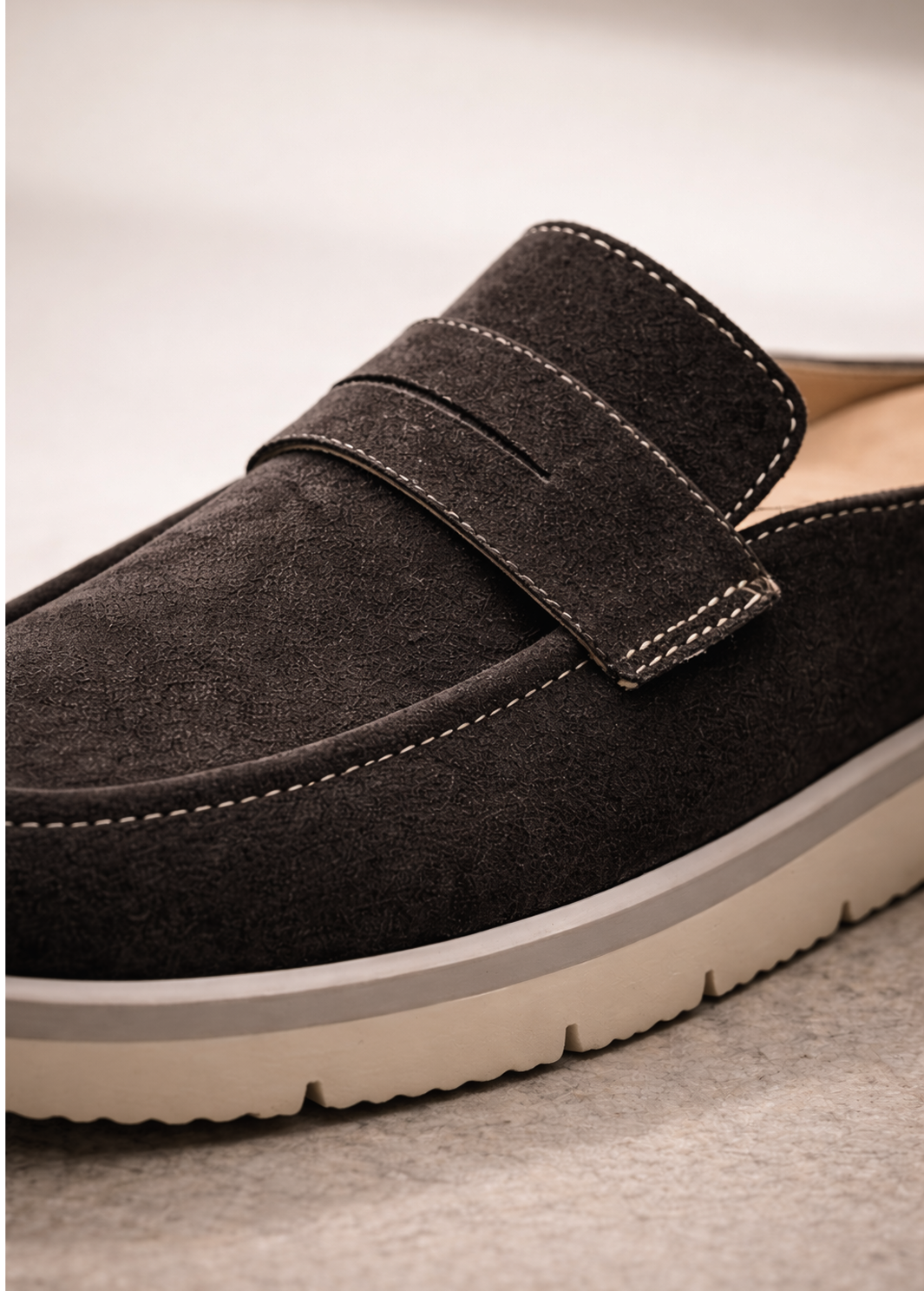 Close-up of dark suede KMRO mule showing apron stitching, strap detail, and cream rubber outsole.