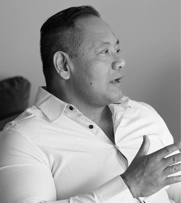Man in a collared shirt speaking and gesturing with his hand, shown in black and white.