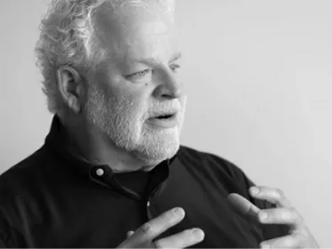 Elderly man with white hair and beard speaking with expressive hand gestures in black and white.