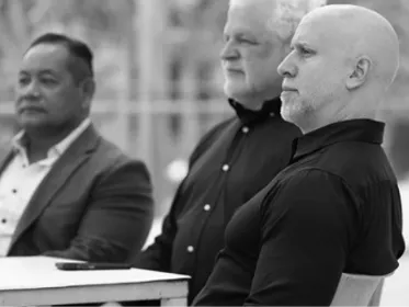Three men sitting side by side, attentively looking towards the right.