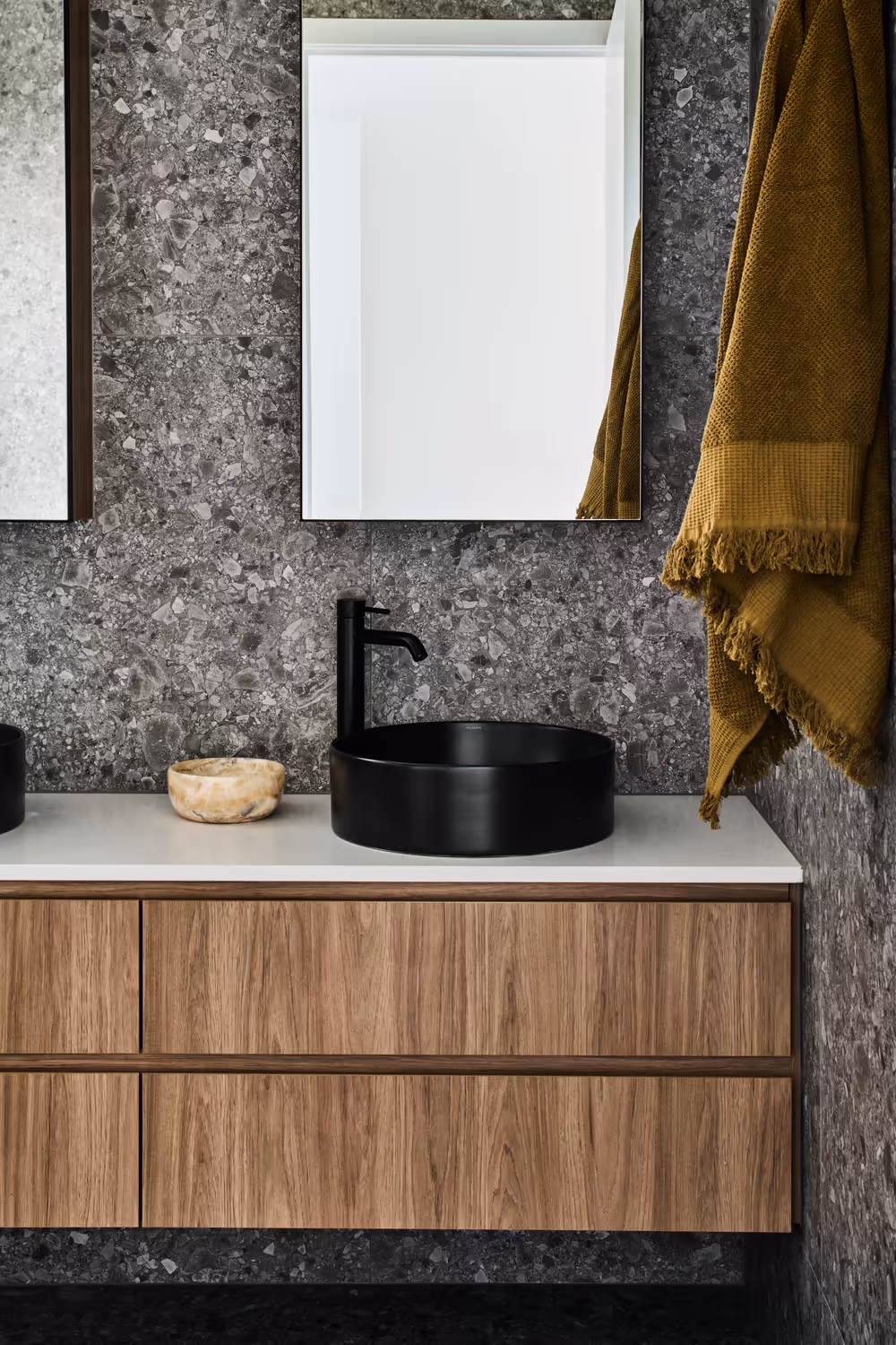 black round basin and tapware on a timber vanity against grey terrazzo tiles, with a mustard towel, opus 4, thornbury