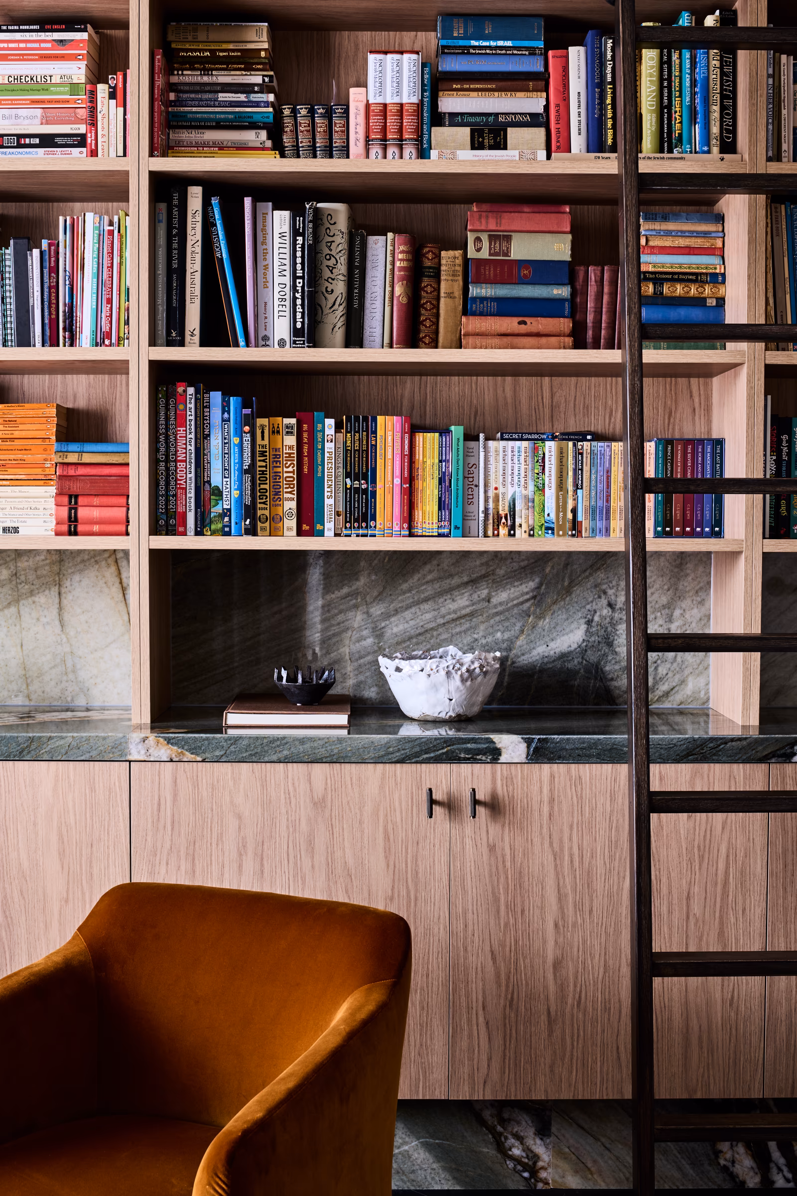 library wall of timber shelving with rolling ladder and green stone ledge, opus 5, caulfield north