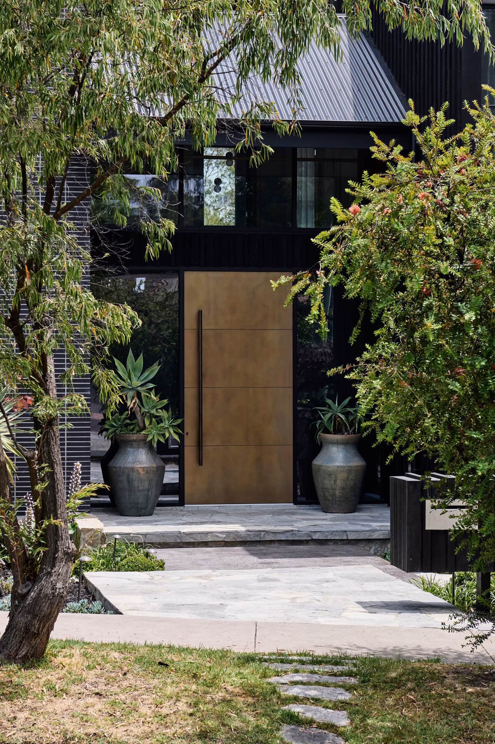 front entry with large bronze-toned door, black cladding and potted succulents on stone steps, opus 2, ashburton