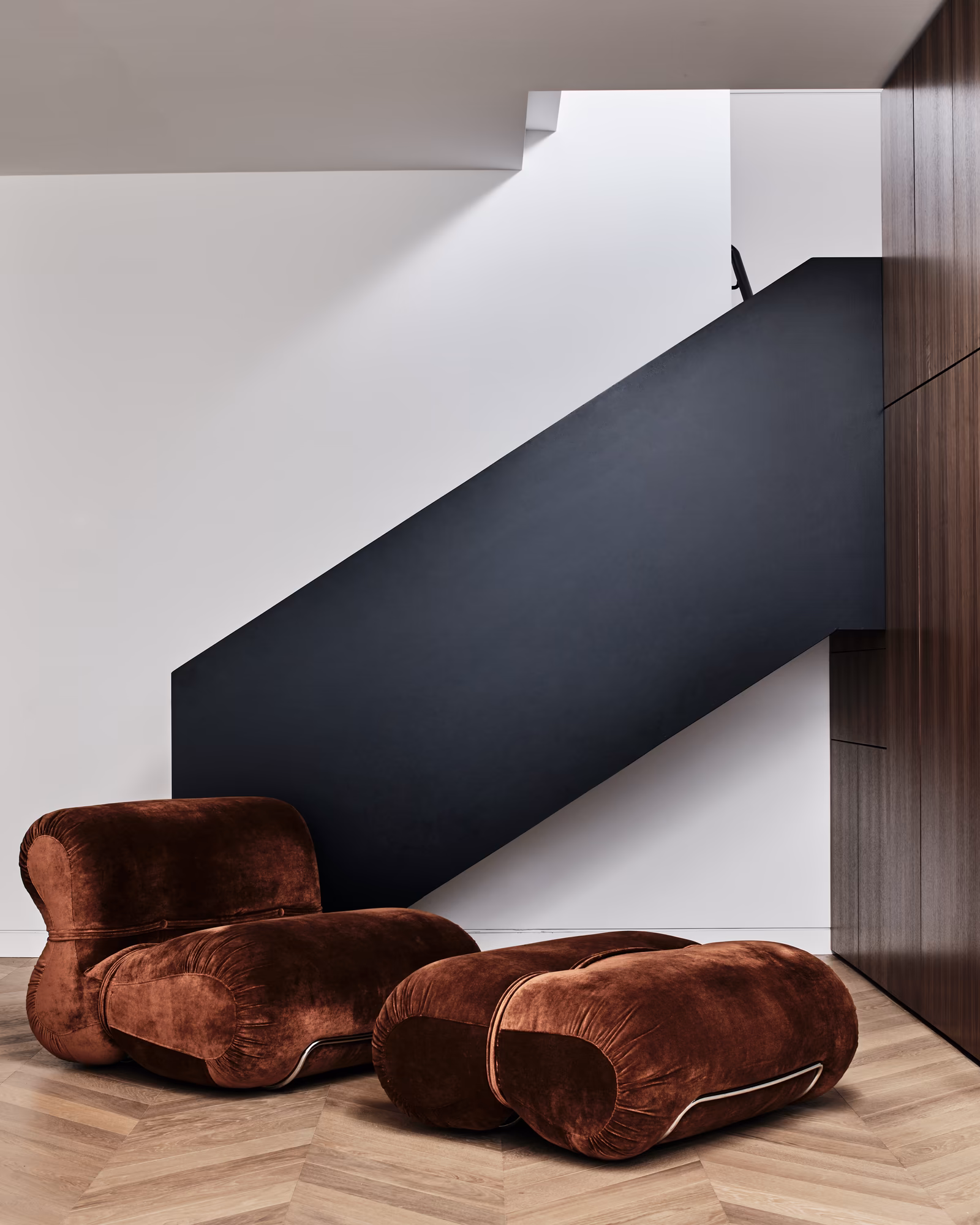 rust velvet lounge chair and ottoman beneath a black steel stair, opus 73, middle park