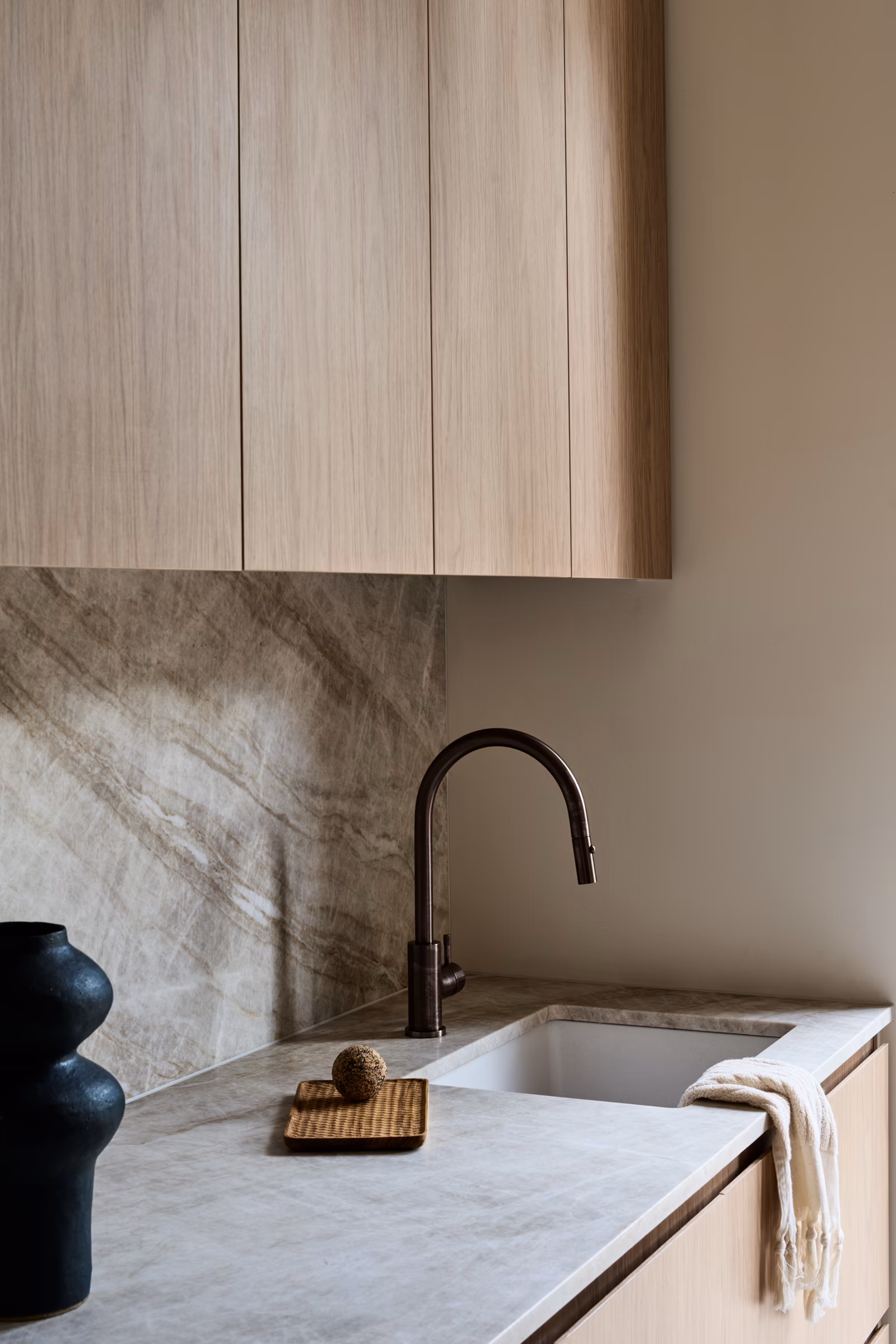 sink detail with veined stone benchtop and splashback, dark tapware and timber cabinetry, opus 5, caulfield north