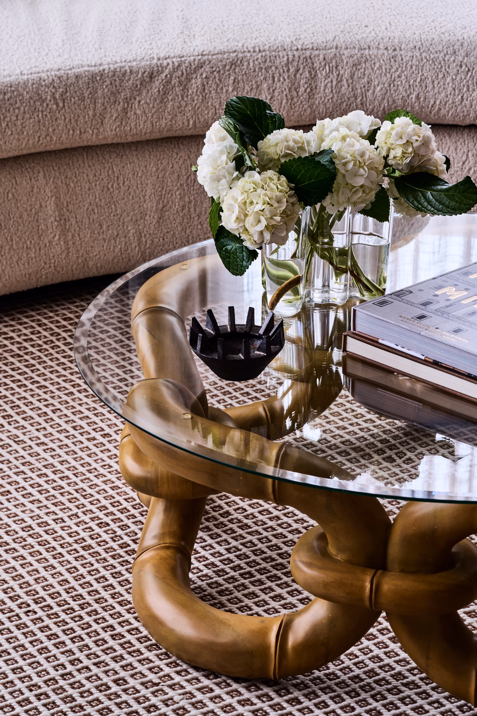 glass-topped coffee table with sculpted timber base and white hydrangeas beside a boucle sofa, opus 5, caulfield north