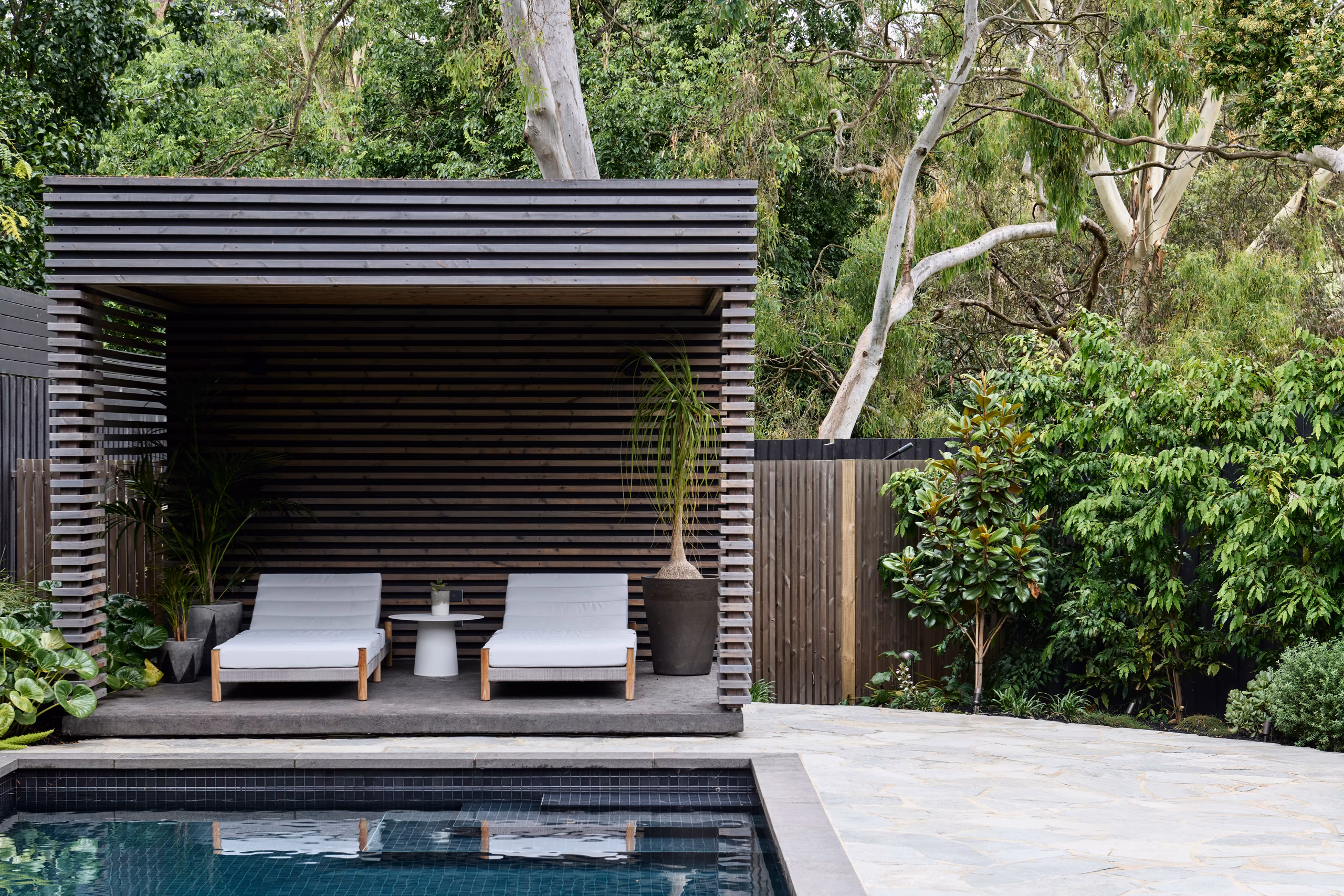 pool with dark tiles and a slatted timber cabana with two sun loungers, opus 2, ashburton