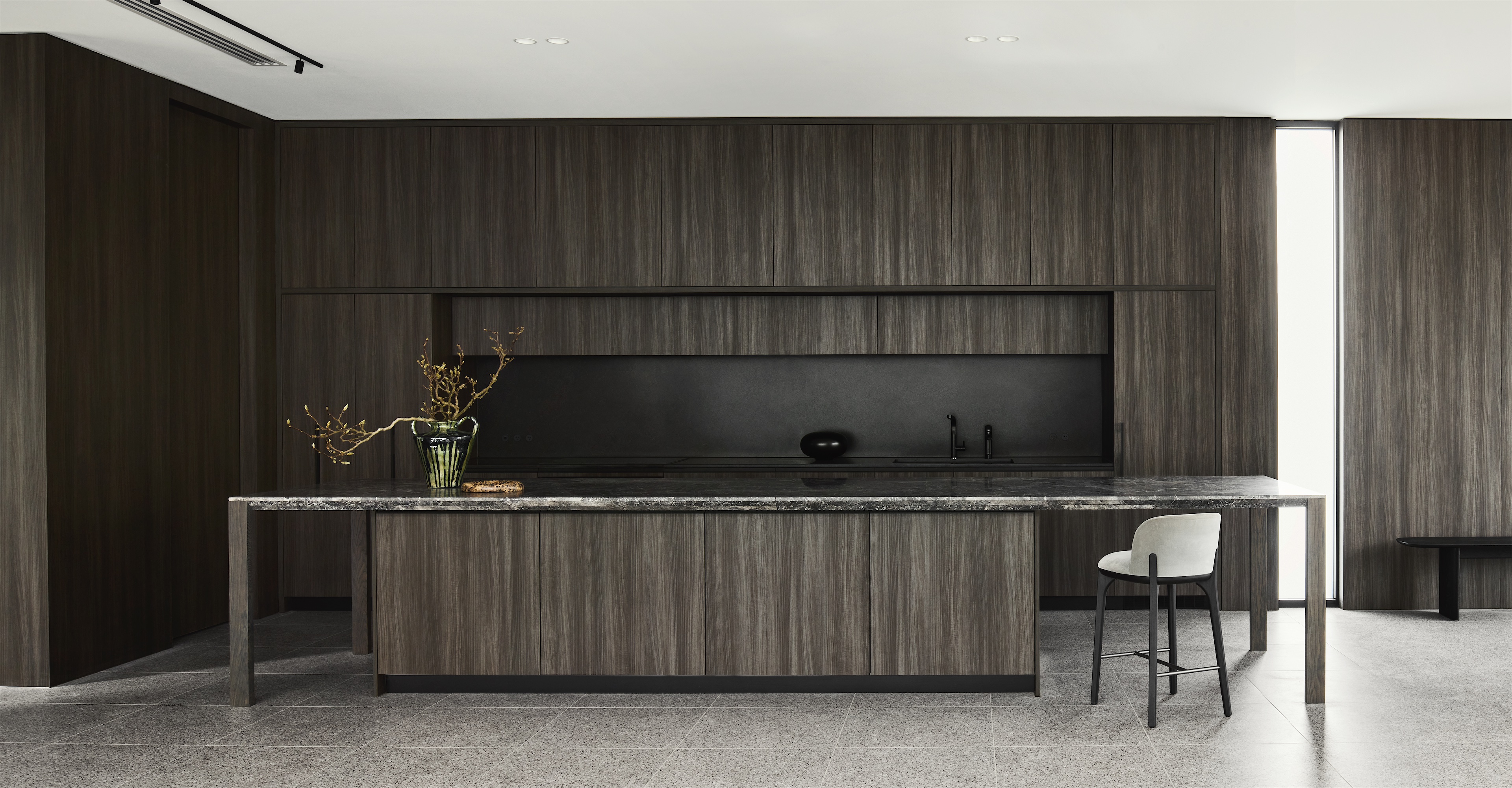 kitchen with long dark stone island, wall of dark timber cabinetry, black splashback and single bar stool, opus 24, ashburton
