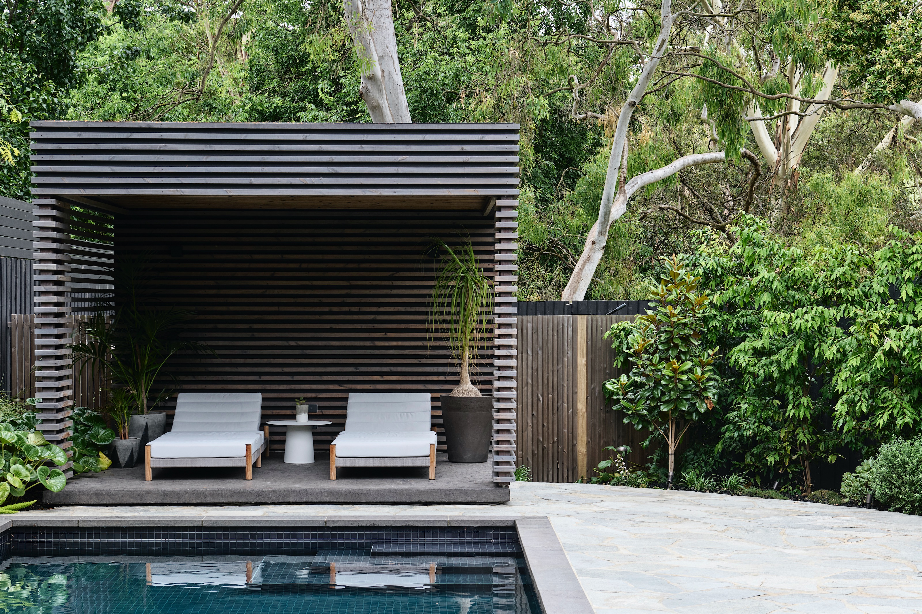 pool with dark tiles and a slatted timber cabana with two sun loungers, opus 2, ashburton