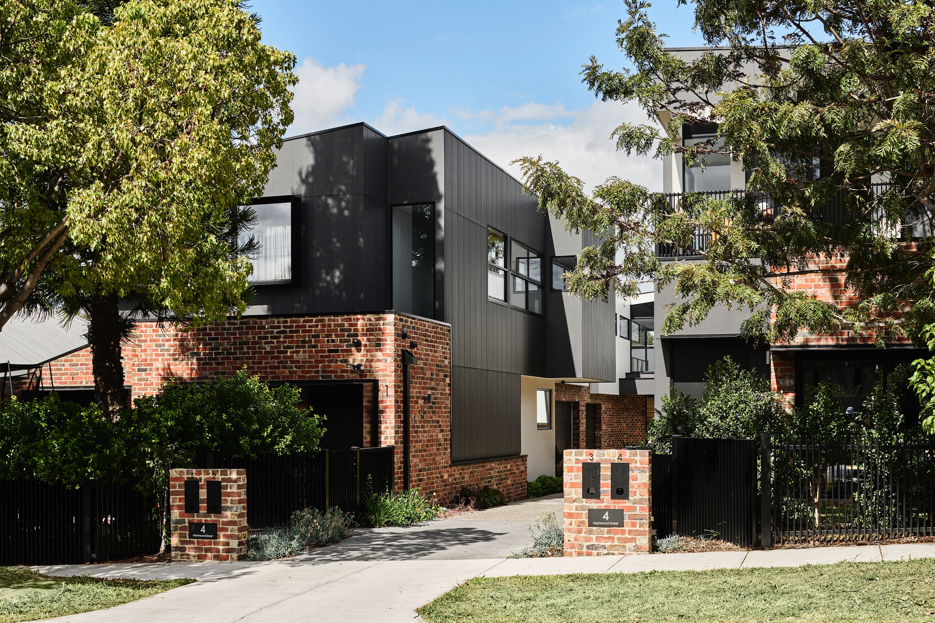 townhouses in red brick and black vertical cladding behind black palisade fencing, opus 4, thornbury